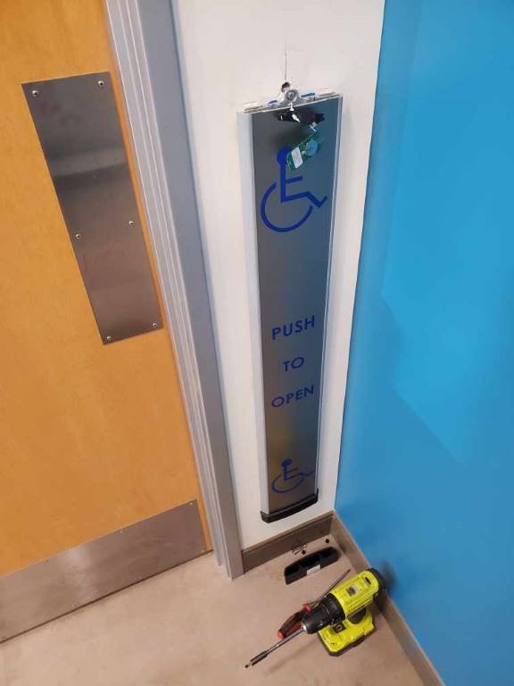 ADA push-to-open accessibility door operator installed by Locks Around the Clock with cordless drill on the floor mid-install